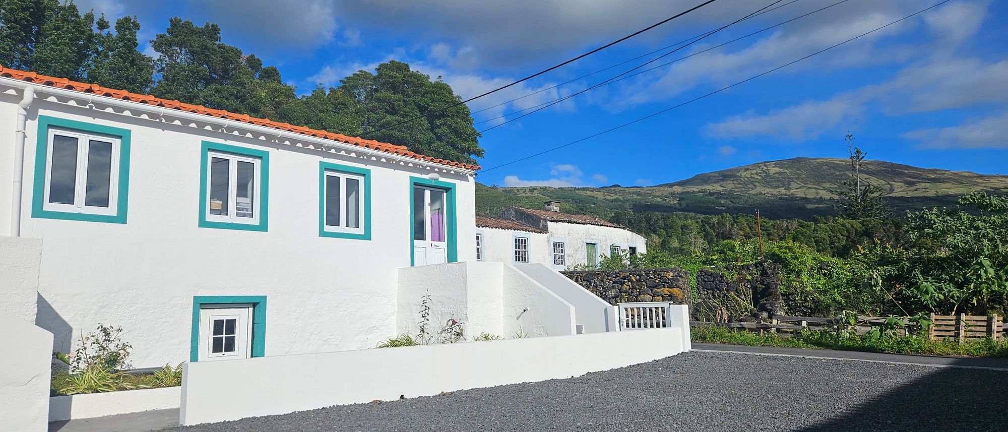 Moradia de fachada branca com molduras verde-água na Silveira, com a encosta da ilha do Pico ao fundo
